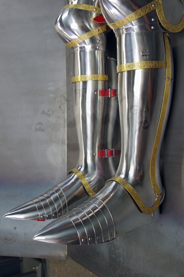 English style leg harness with fully closed cuisses, full greaves with characteristic line around outside ankles. Demi-greaves connected with greaves on rotary pin. Made of medium carbon steel of various thickness from 1 mm up to 1,5 mm. Heat hardened and tempered up to 42 HRC. Brass bands decoration motive based on example visible on Henry V tournament helm. Hand made steel buckles in set./Osony ng w stylu angielskim z w peni zamknitymi nabiodrkami, nagolennicami z charakterystyczn lini wok zewntrznej kostki. Demi-greave poczony z nagolennicami poprzez obrotowy pin. Wykonane ze stali redniowglowej rnej gruboci od 1 mm do 1,5 mm. Hartowane i odpuszczane do 42 HRC. Mosine listwy dekoracyjne z motywem wzorowanym na hemie turniejowym Henryka V. W zestawie rcznie robione sprzczki stalowe.